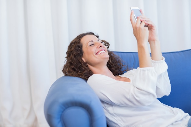 Donna sorridente che si siede sul divano e usando il suo smartphone