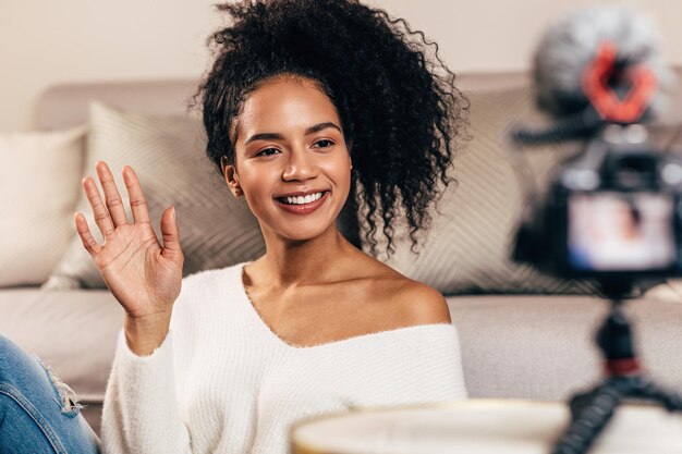 Smiling woman sitting at home while gesturing against camera