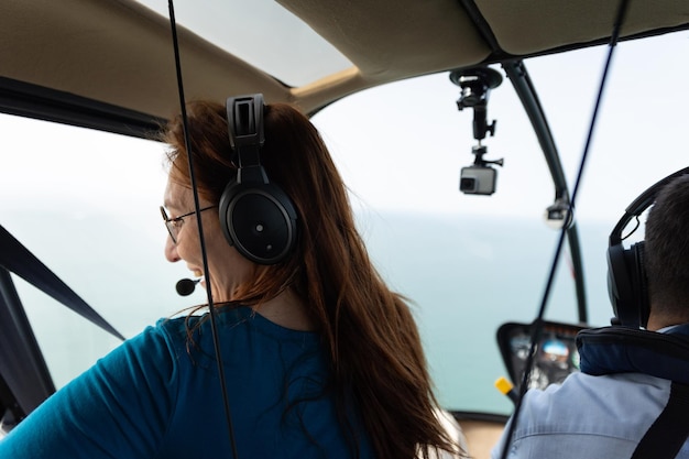 Улыбающаяся женщина сидит на пассажирском сиденье вертолета и смотрит в окно