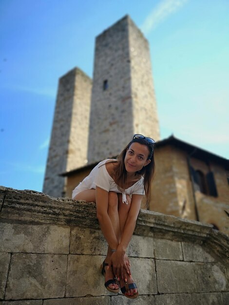 Foto donna sorridente seduta sul muro di sostegno