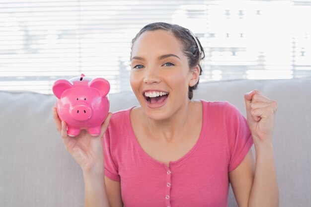 Photo smiling woman sitting on sofa and holding piggy bank