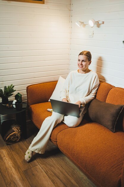 smiling woman sitting on sofa at home and talking on phone working on laptop online freelancer modern lifestyle