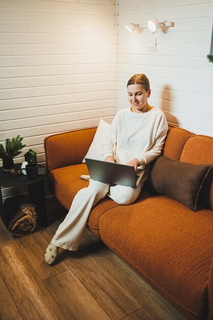 smiling woman sitting on sofa at home and talking on phone working on laptop online freelancer modern lifestyle
