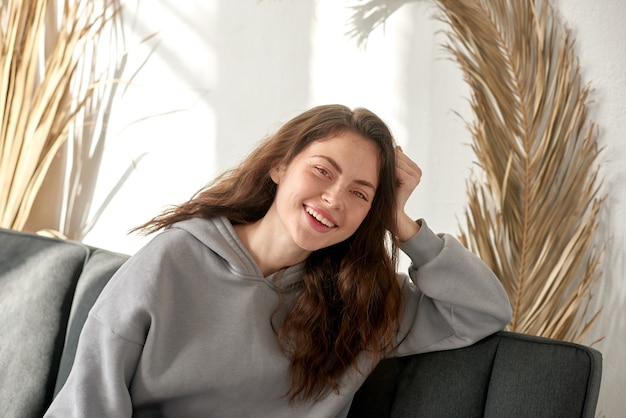 Smiling woman sitting on sofa and making face time video calling at home, social distancing