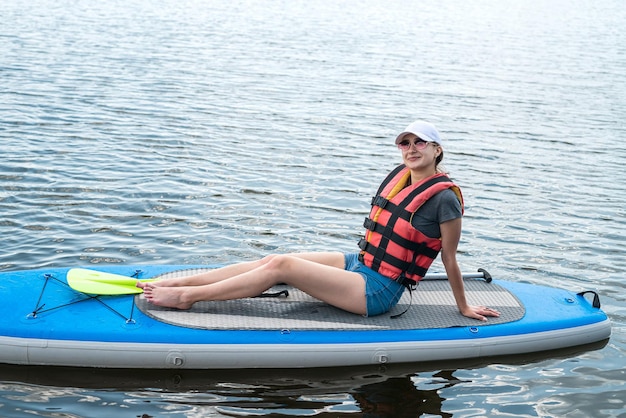 Smiling woman sitting on sup board with paddle