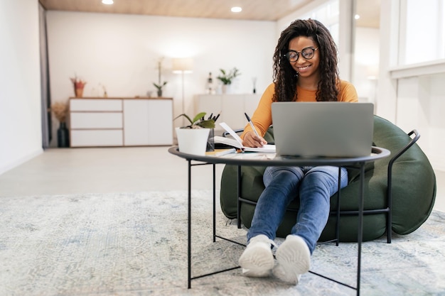 Donna sorridente che si siede al tavolo usando il computer che scrive nel taccuino