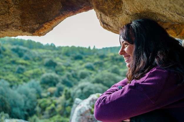 Donna sorridente seduta sulla cima di una collina a guardare il paesaggio