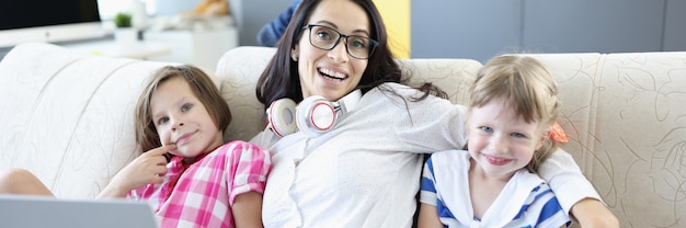 ノートパソコンとソファの上の子供たちと一緒に座っている笑顔の女性。