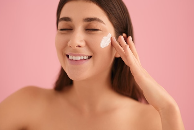 Photo smiling woman smearing cream on cheek in studio