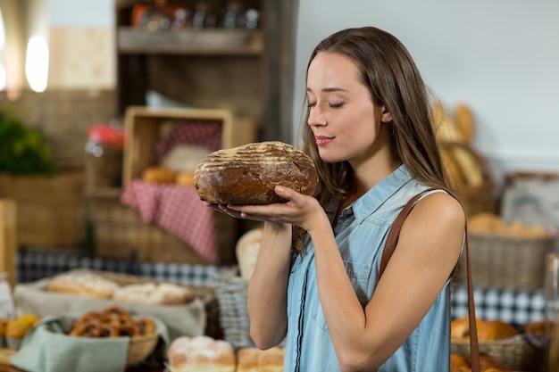 Donna sorridente che sente l'odore di una pagnotta di pane al bancone