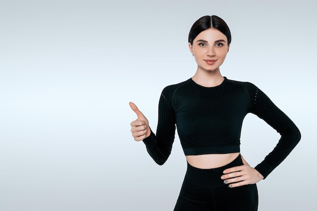 Smiling woman in sportswear showing okay thumb up hand sign or gesture isolated