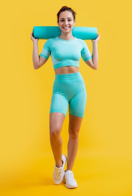 운동복을 입은 미소 짓는 여성, 운동 매트, 스튜디오에서 운동하는 여성, 운동옷을 입은 여성, 노란색 배경에 고립된 운동 매트