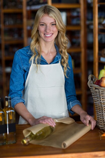 Smiling woman staff wrapping olive oil bottle with brown paper