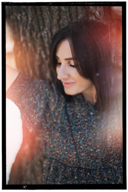 Photo smiling woman standing against tree trunk