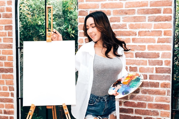 Photo smiling woman standing by canvas at studio