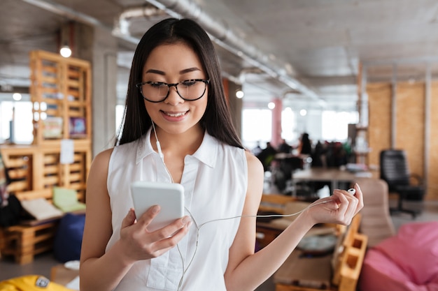 Smiling woman standing and listening to music from cell phone