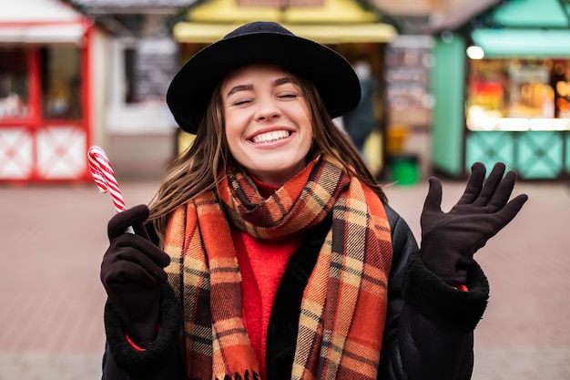 Smiling woman standing outside on winter fair market hold striped candy