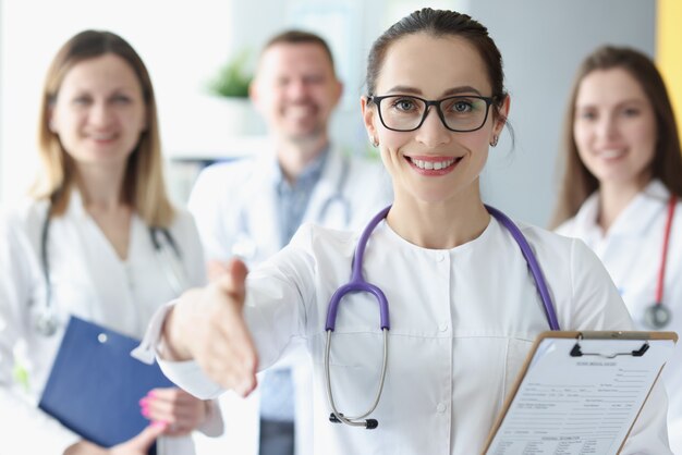 Smiling woman stretches out her hand for handshake behind her team of doctors