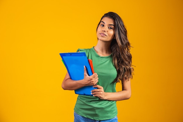 Smiling woman student with school books in hands on yellow background.