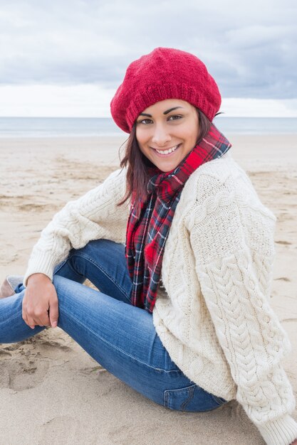 세련 된 따뜻한 옷을 입고 해변에 앉아 웃는 여자