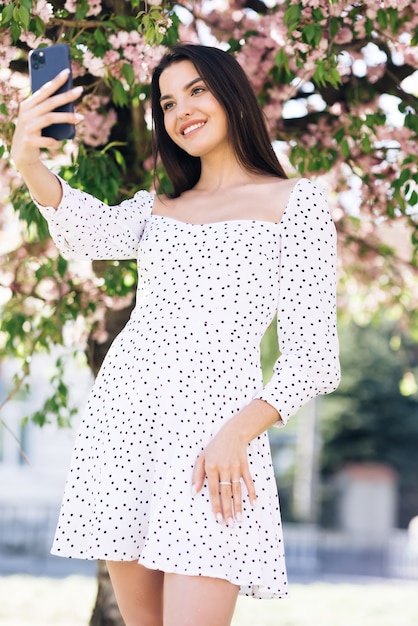 smiling woman in summer white dress taking selfie self portrait photos on smartphone