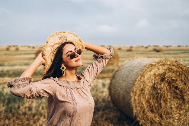 Smiling woman in sunglasses with bare shoulders on a wheat field and bales of hay