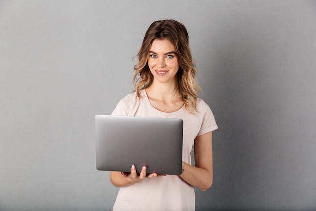 Photo smiling woman in t-shirt holding laptop computer over grey