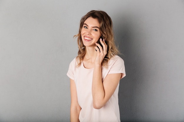 Smiling woman in t-shirt talking by smartphone and over grey