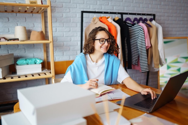 Smiling woman takes notes of orders from with laptop Dropshipping owner works