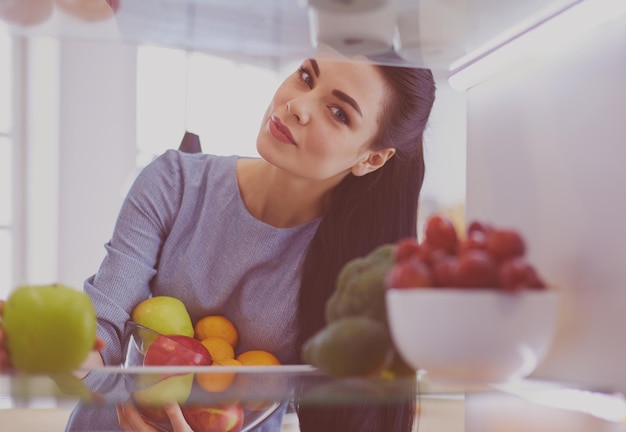 冷蔵庫の健康食品の概念から新鮮な果物を取り出して笑顔の女性