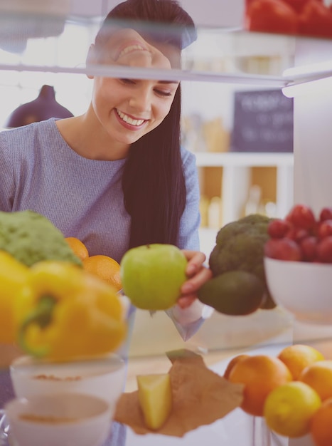 Smiling woman taking a fresh fruit out of the fridge healthy food concept