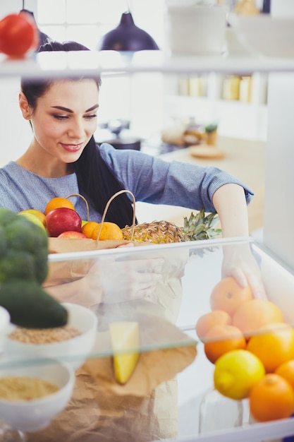 冷蔵庫から新鮮な果物を取り出して笑顔の女性、健康食品のコンセプト