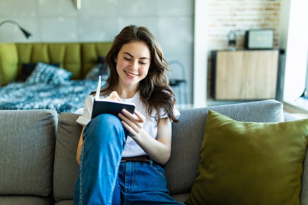 Smiling woman taking notes on her couch at home