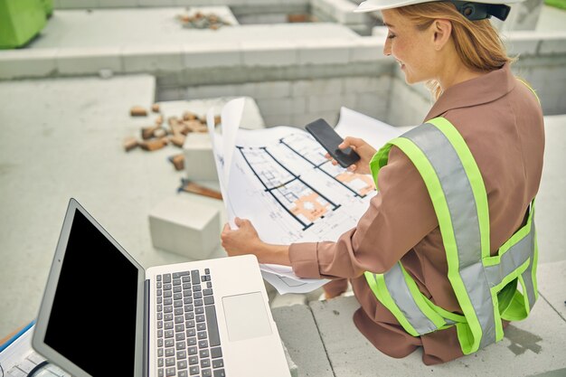 smiling woman taking photos of a house plan with her smartphone