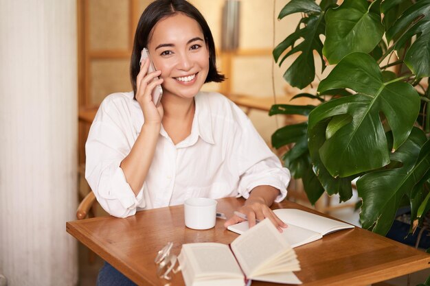Smiling woman talking on mobile answer phone call and looking\
happy sitting in cafe
