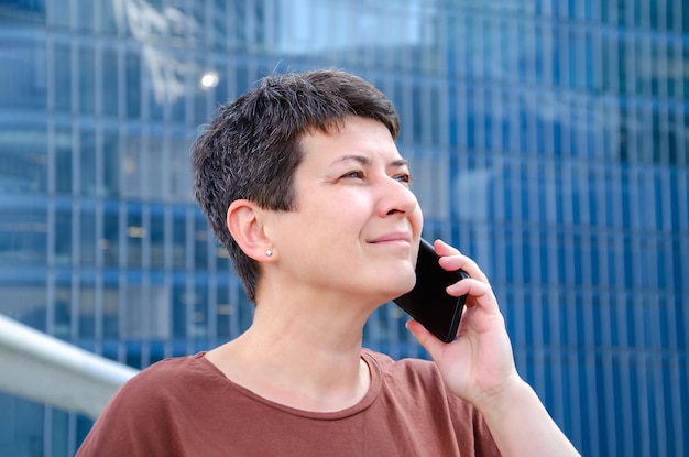 Smiling woman talking on smartphone in background of highrise building with a blue glass facade