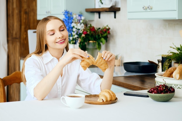 Smiling woman tears apart a fresh croissant