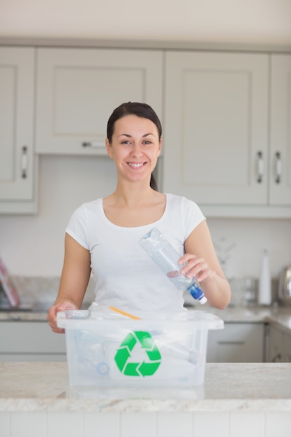 Smiling woman throwing bottle into recycling bin