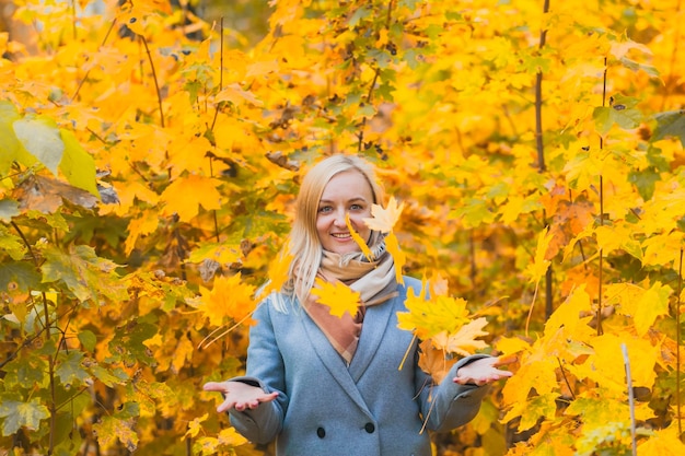 A smiling woman tossed up a bunch of leaves in a park against a background of trees. Authentic 40-year-old woman without retouching