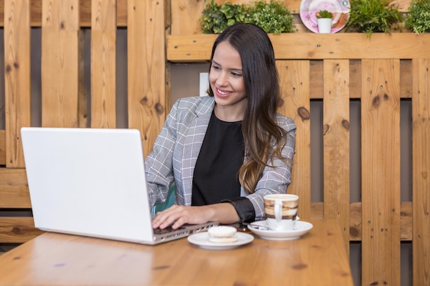 Smiling woman typing on laptop and having coffee and dessert