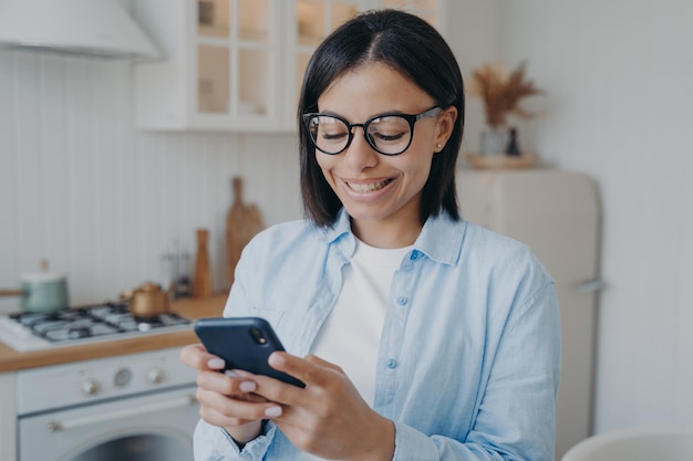 Smiling woman use mobile phone apps order groceries in online\
store check social networks at home