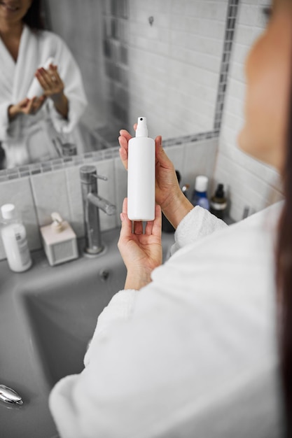 Photo smiling woman using cosmetics spray in bathroom