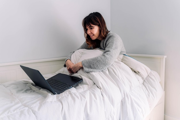 Smiling woman using laptop on bed at home