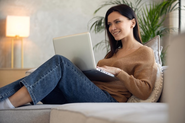 Smiling woman using laptop sitting on couch at home freelancer working on computer project