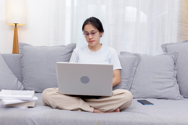 Smiling woman using laptop sitting on couch at home. Women sitting on sofa use laptop shopping, chat online on social network. Women working at home with computer at living room