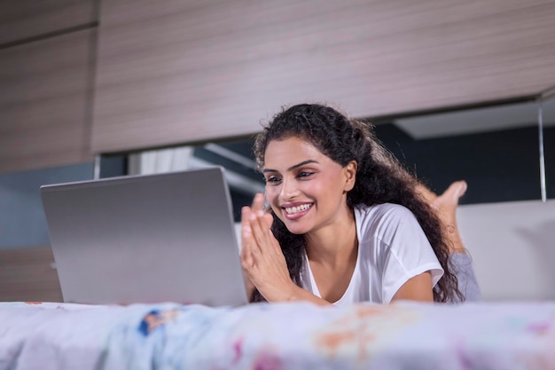 Photo smiling woman using laptop while lying on bed