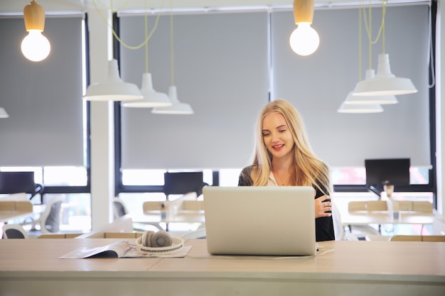 Smiling woman using laptop in work place for small businesses looking to engage audiences and scale content creation can adopt new marketing technology in workspace. Freelancer concept.