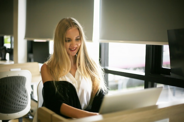 Smiling woman using laptop in work place for small businesses looking to engage audiences and scale content creation can adopt new marketing technology in workspace. Freelancer concept.