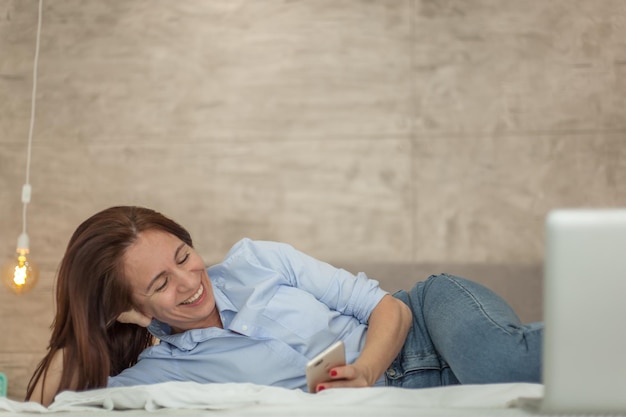 Photo smiling woman using mobile phone on bed