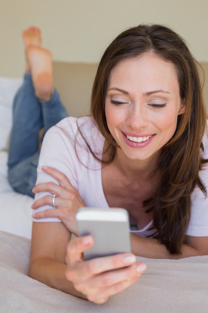 Smiling woman using mobile phone in bed